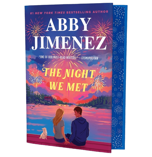 Book cover of 'The Night We Met' by Abby Jimenez with a couple and dog by a lake at sunset.